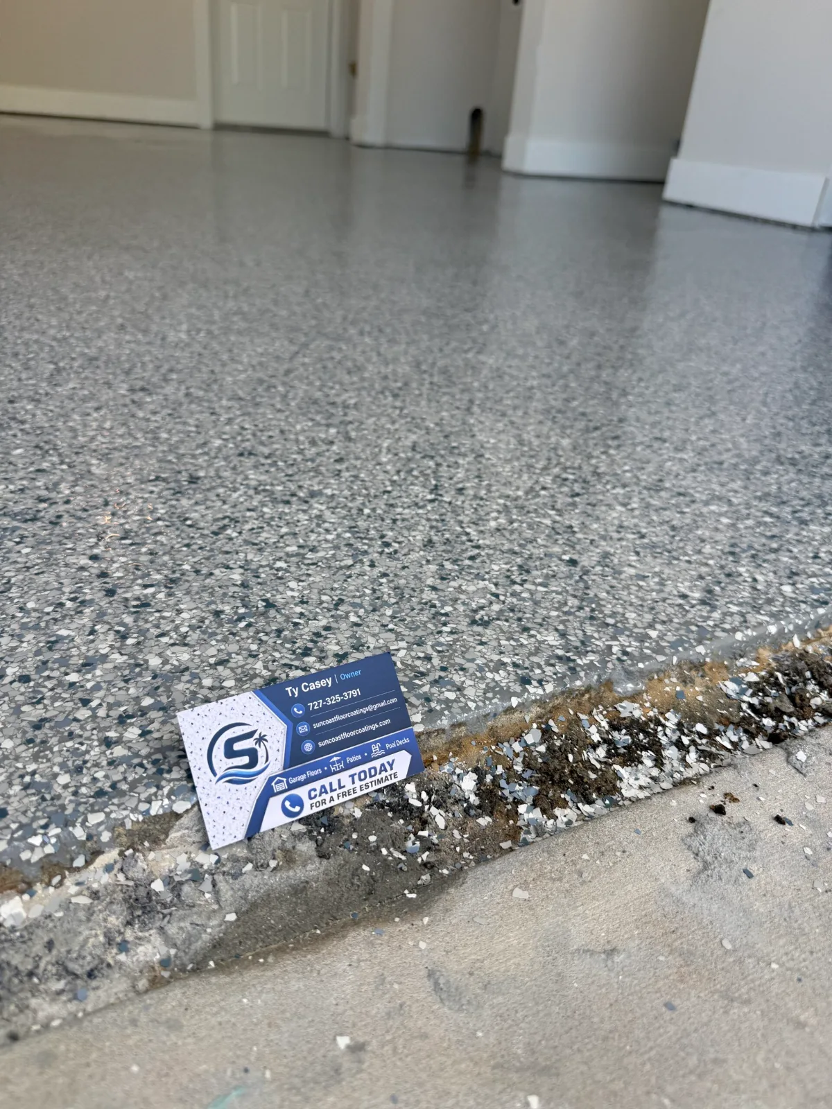 Close-up of gray-blue full-flake garage floor coating texture at garage threshold with Suncoast Floor Coatings card